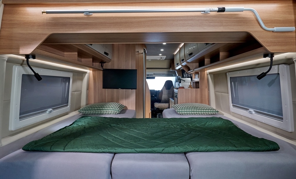 Zwei Längsbetten mit grüner Bettwäsche und Panoramafenstern im VANTURA Campervan Der Entdecker