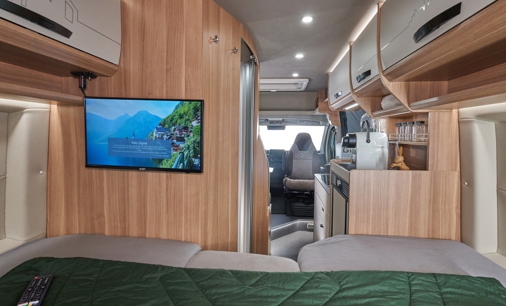 Bett mit Blick über den wandmontierten TV bis zur Küche