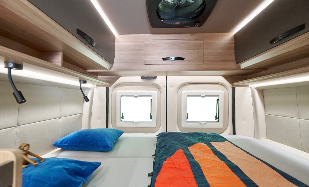 Blick auf das feste Querbett im VANTURA Campervan Der Wanderer mit zwei Fenstern und indirekter LED-Beleuchtung