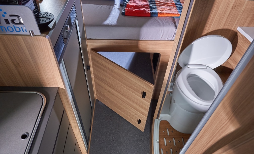 Offene Kassettentoilette neben Stauraum im Badbereich des Campervans