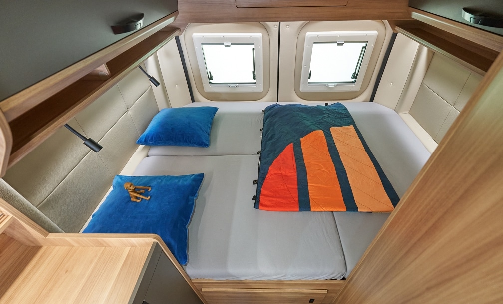 Nahaufnahme des Querbetts 196 x 140 cm mit blauen Kissen und Decke im Peugeot Boxer Campervan